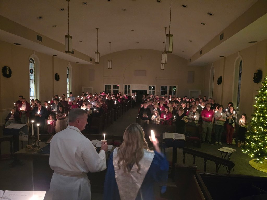 A candlelit sanctuary seen from the chancel, with the Christmas tree glowing