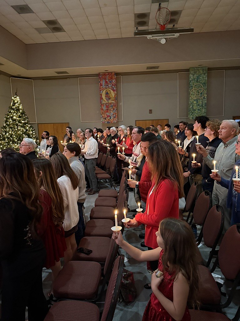 Worshipers holding candles in Hammill Hall beside a lit Christmas tree